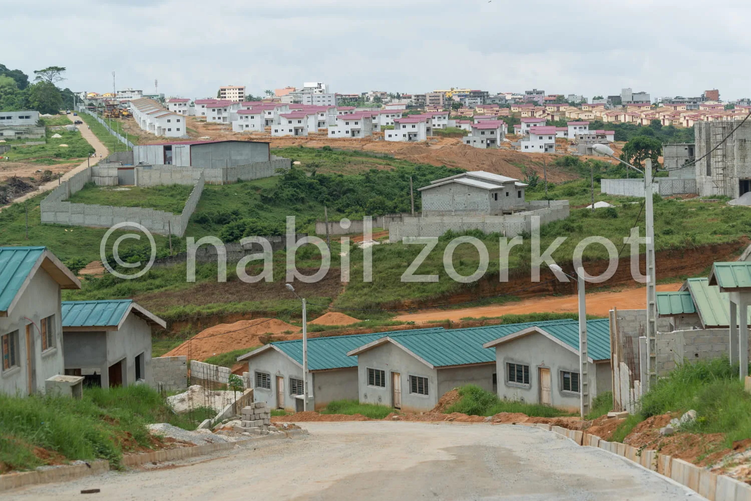 Africa photo — Image montrant un quartier résidentiel en construction sur une colline. Au premier plan, quatre petites maisons individuelles avec toit