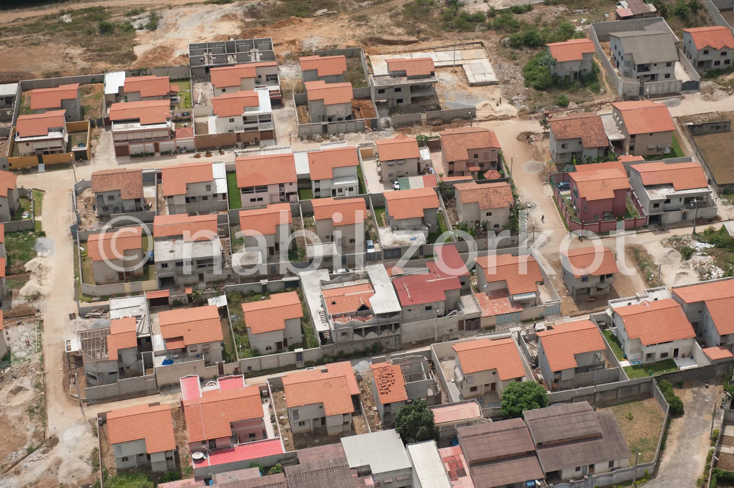 Africa photo — Image aérienne montrant un quartier en développement avec plusieurs maisons individuelles aux toits orange et rouges, des rues en forma