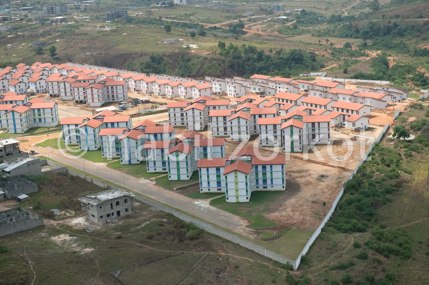 Africa photo — Vue aérienne d’un lotissement en cours de construction avec plusieurs immeubles de 3 étages aux toits rouges, entourés de routes et d’e