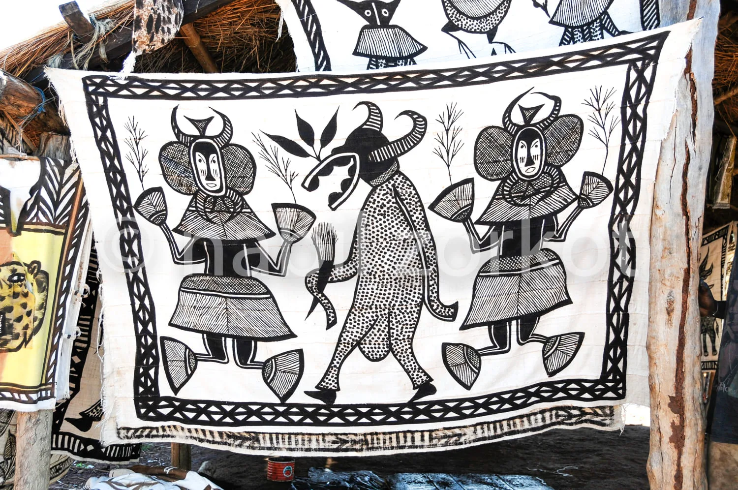 Africa photo — Un tissu artisanal représentant deux personnages stylisés en costume traditionnel, entourés de deux buffles aux cornes imposantes, le t