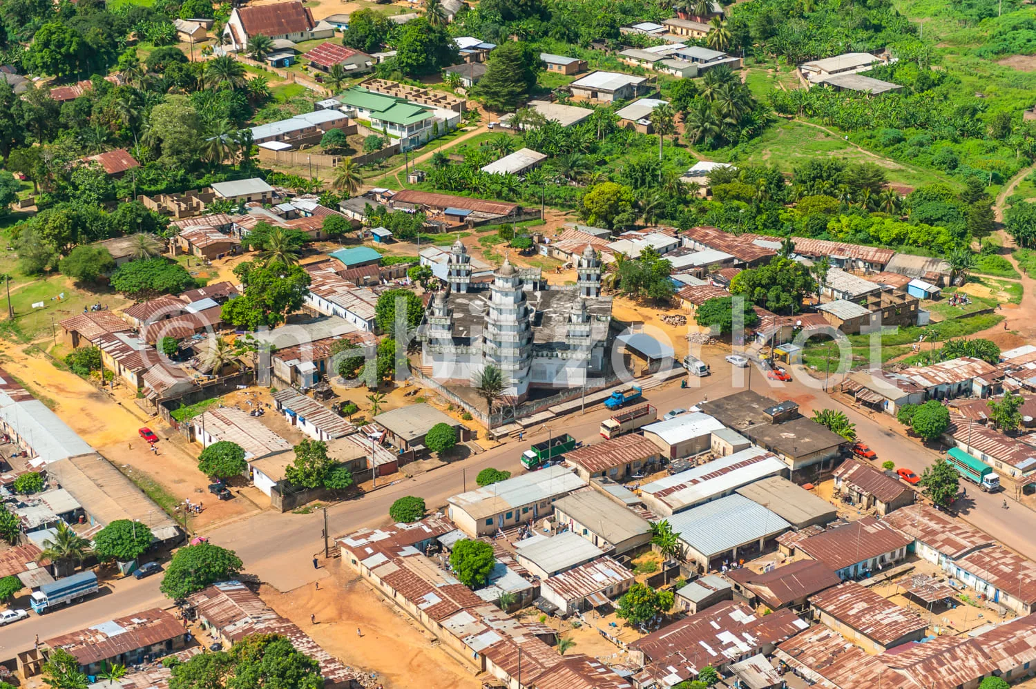 Africa photo — Vue aérienne d’un village tropical avec une église en pierre grise au centre, entourée de maisons aux toits colorés et de végétation de