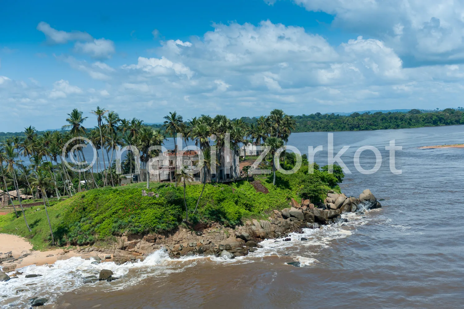 Africa photo — Vue aérienne d’une plage de sable bordée de palmiers, avec des vagues qui déferlent sur des rochers, une végétation luxuriante en arriè