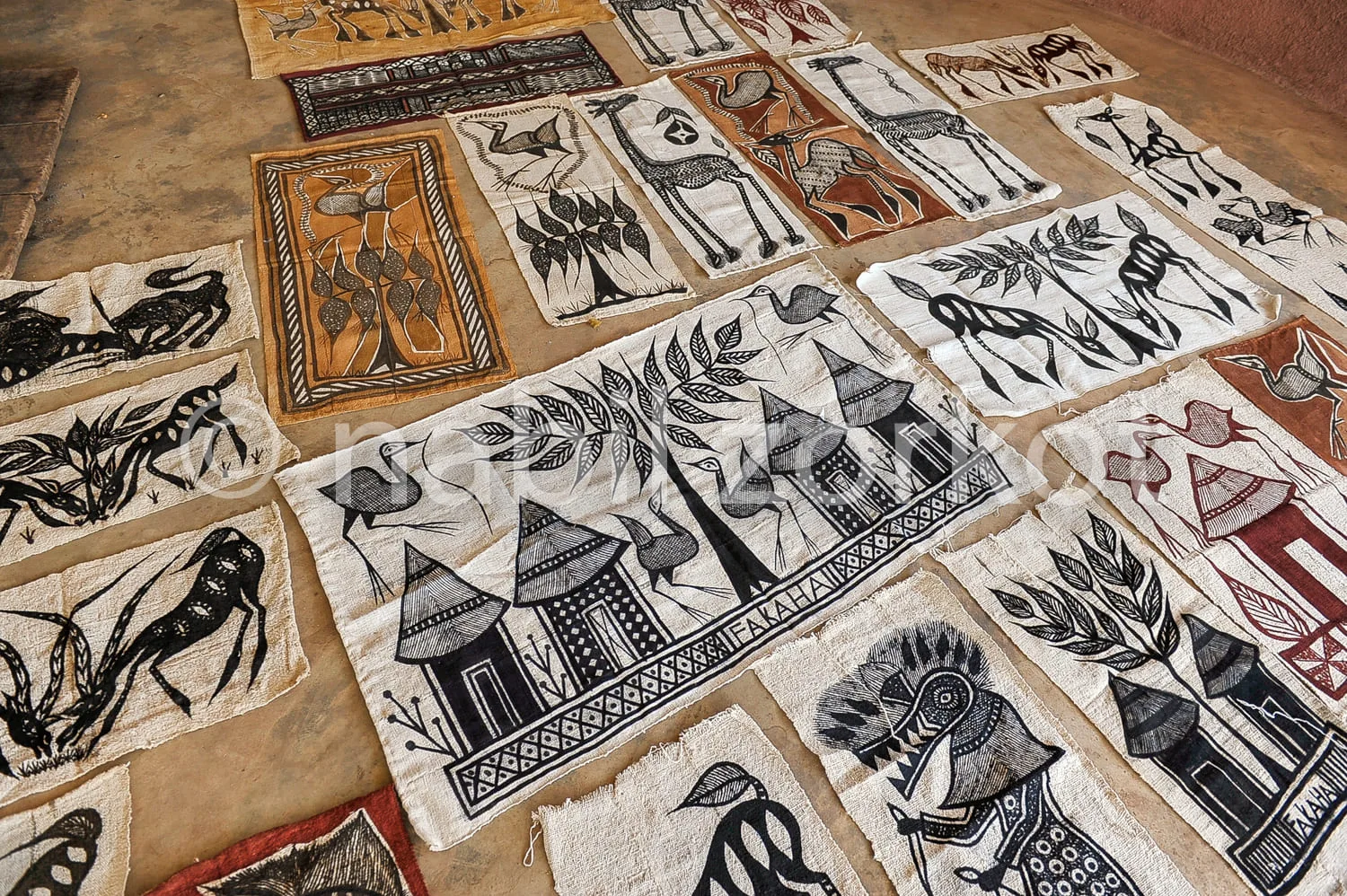 Africa photo — Une collection de tissus artisanaux disposés sur une surface plane, représentant des motifs variés d'animaux comme des chevaux, des ois