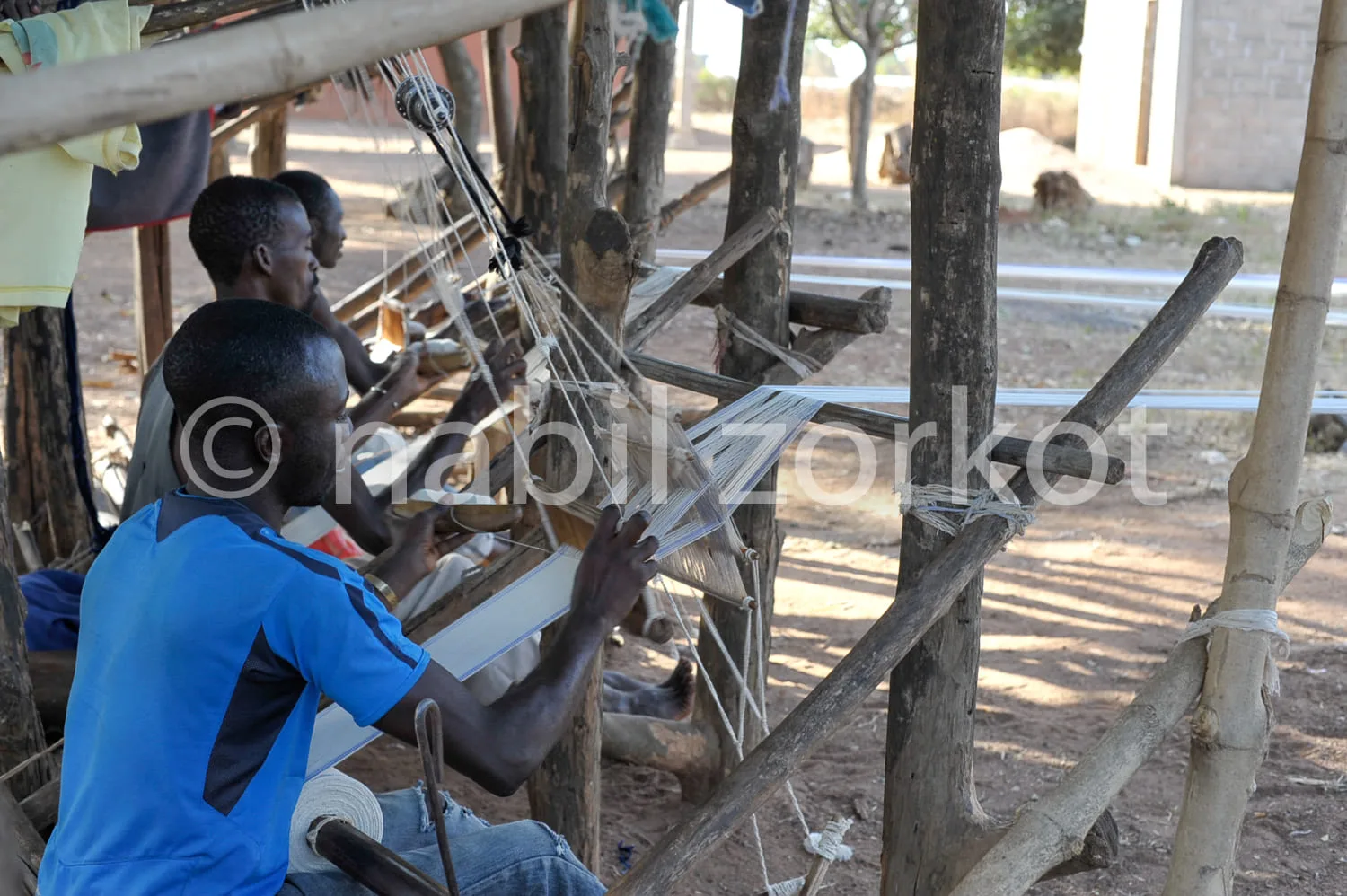 Africa photo — Deux personnes assises sous une structure en bois et bambou, travaillant ensemble à la fabrication de paniers en fibres végétales avec