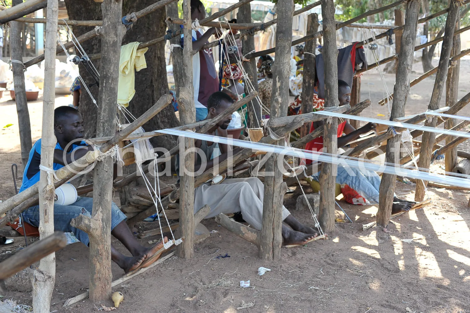 Africa photo — Une structure en bois rudimentaire abritant plusieurs personnes assises ou allongées sur des hamacs suspendus entre les troncs, avec de