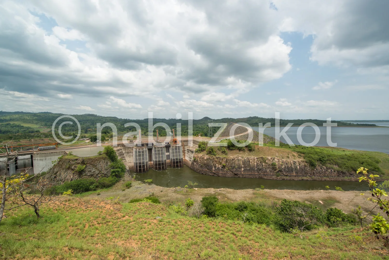 Africa photo — Vue d’un barrage hydroélectrique situé en bordure d’un lac, avec des portes métalliques visibles au centre, entouré de végétation verte