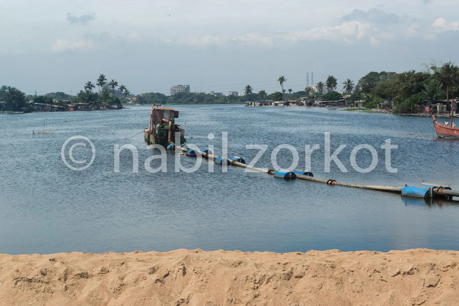 Africa photo — Un bateau de pêche coloré amarré à un ponton flottant bleu et noir sur un fleuve calme, entouré de végétation tropicale et de maisons e