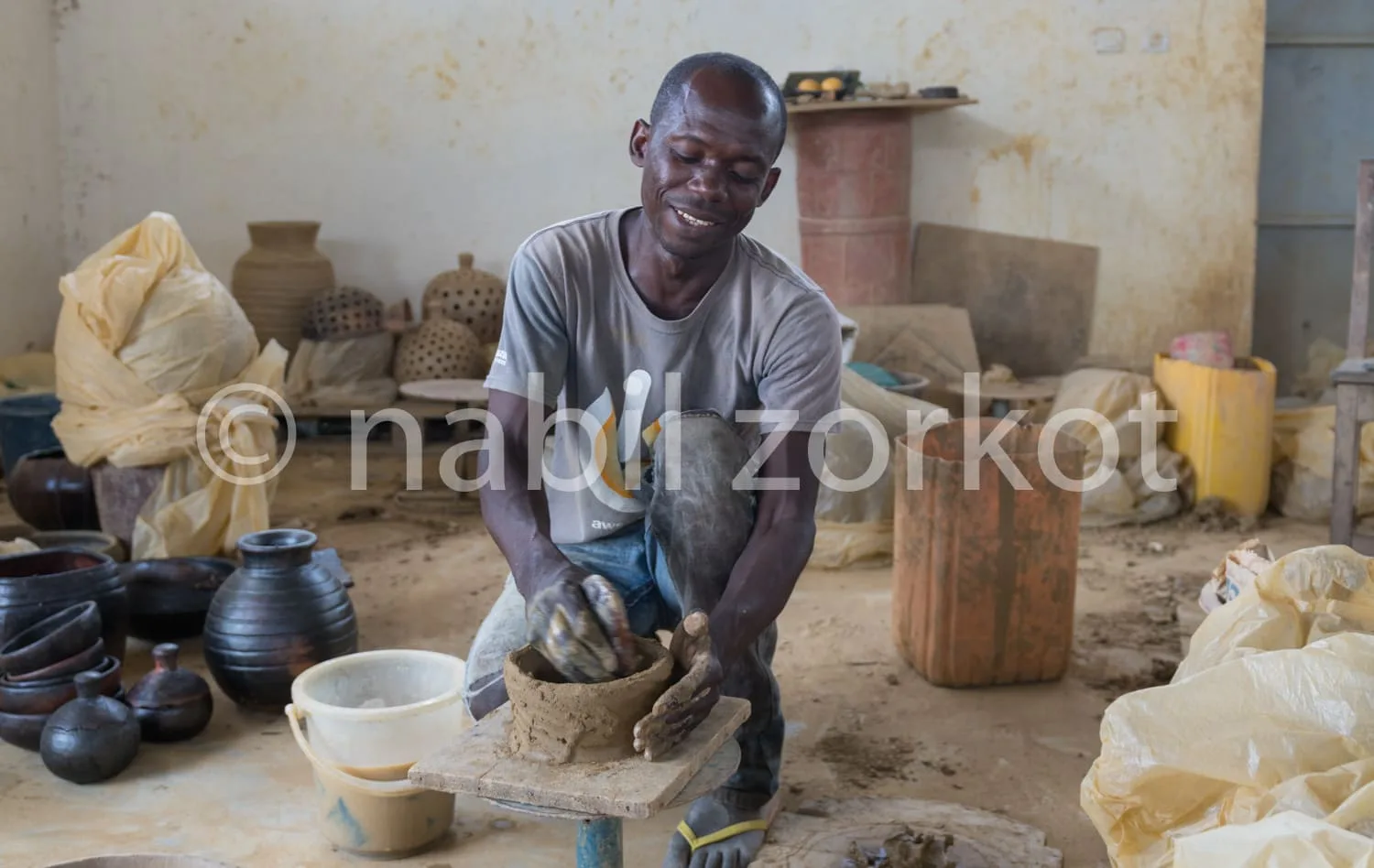 Africa photo — Un artisan souriants façonne soigneusement une pièce de poterie sur un tour de potier dans un atelier rempli d’outils et de créations e
