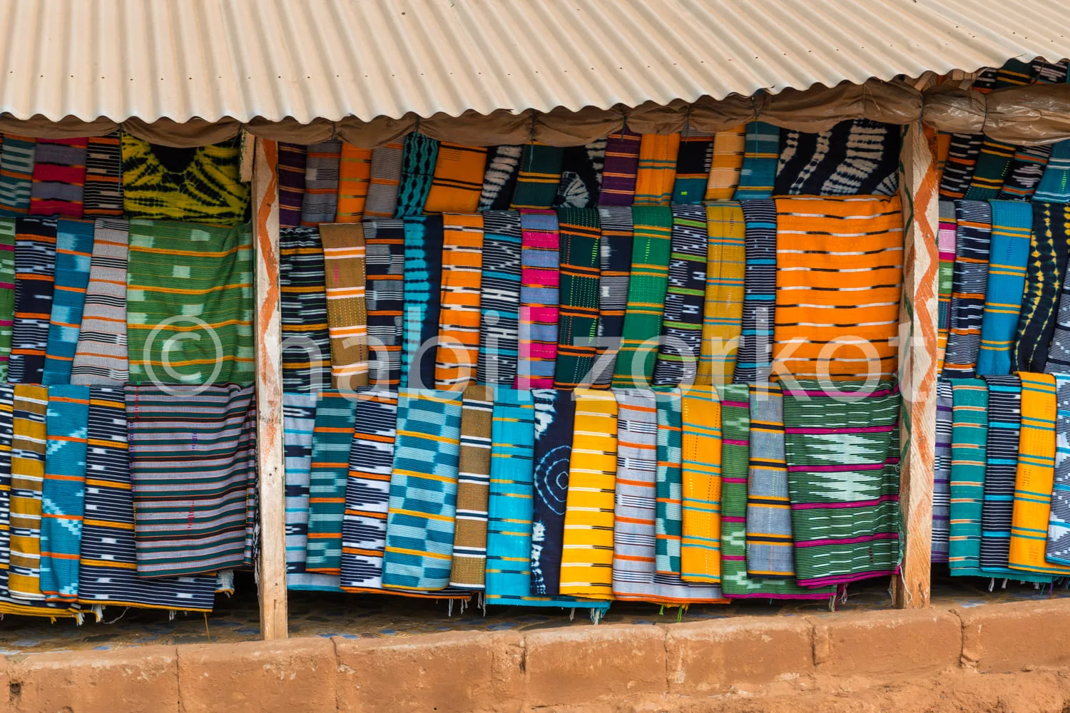 Africa photo — Une rangée de tissus artisanaux aux motifs variés et aux couleurs vives, principalement des rayures horizontales dans des tons bleus, v