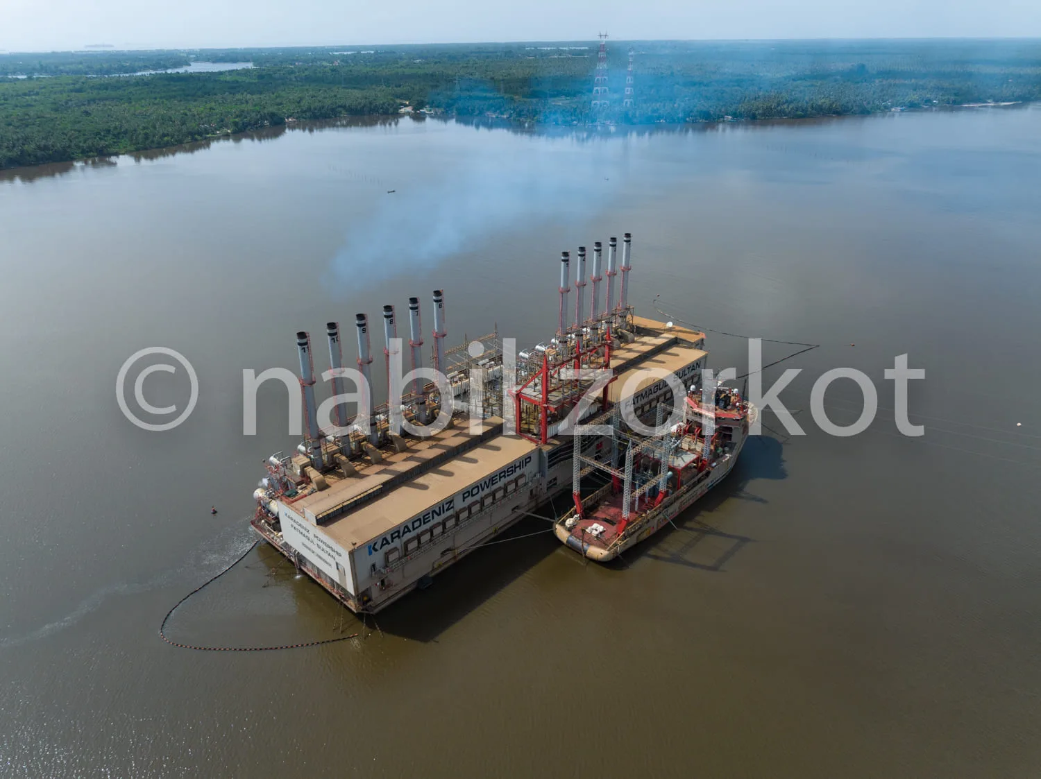 Africa photo — Un navire industriel flottant sur un large fleuve, équipé de plusieurs cheminées verticales et de structures métalliques, entouré d’eau