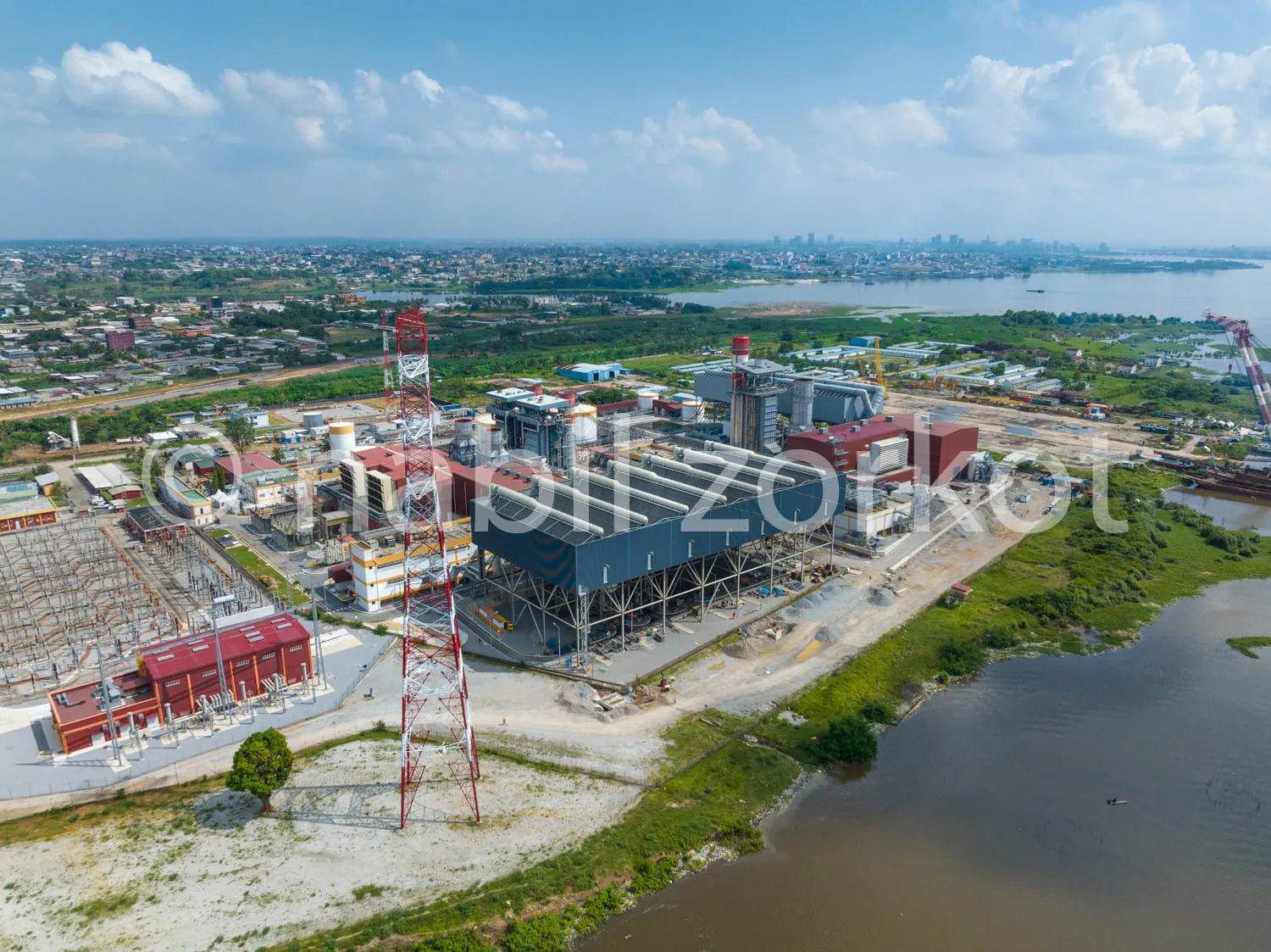Africa photo — Vue aérienne d’une centrale électrique industrielle avec des bâtiments métalliques bleus et rouges, des cheminées et des lignes électri
